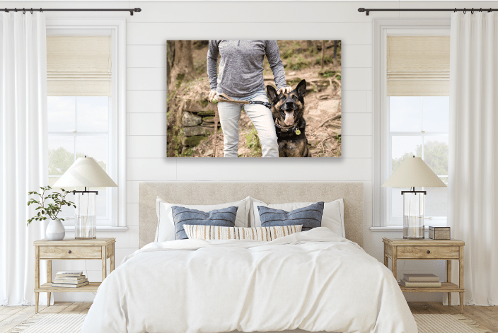 Large canvas showing a German Shepherd standing next to his owner whose hand is resting on his head.  The canvas hangs over a bed in a bedroom.
