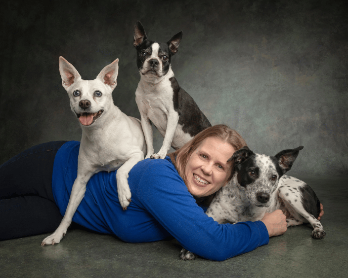 A woman lying on the ground in a blue shirt with 3 dogs surrounding her