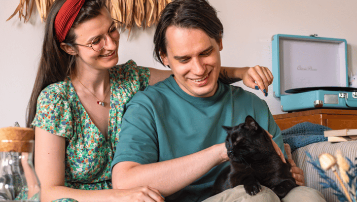 Couple loving their black cat on couch